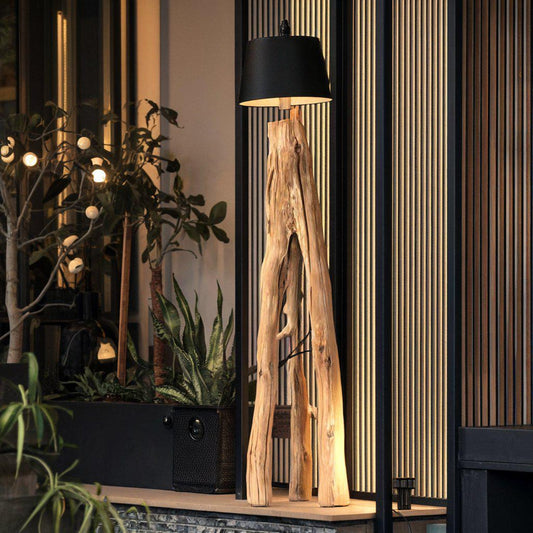 A rustic natural‑wood floor lamp made from a tree trunk, styled in a corner with a black lampshade combining organic texture with warm ambient lighting in minimalist or farmhouse interiors